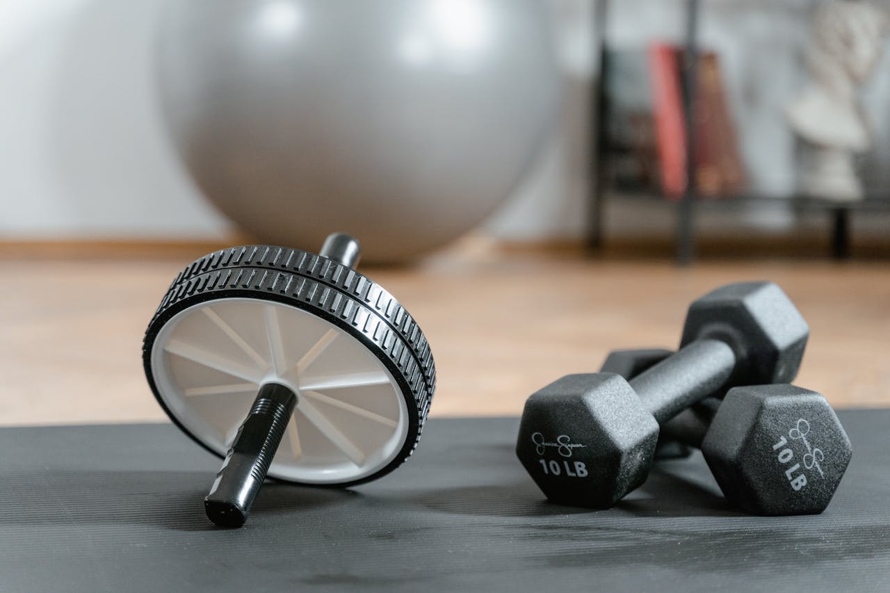 about-01 Close-up of ab wheel and dumbbells on a mat in a home gym setting.
