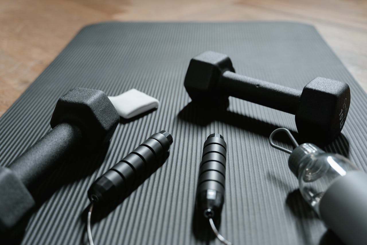 services-02 Close-up of dumbbells, jump rope, and water bottle on a yoga mat, ideal for home fitness routines.
